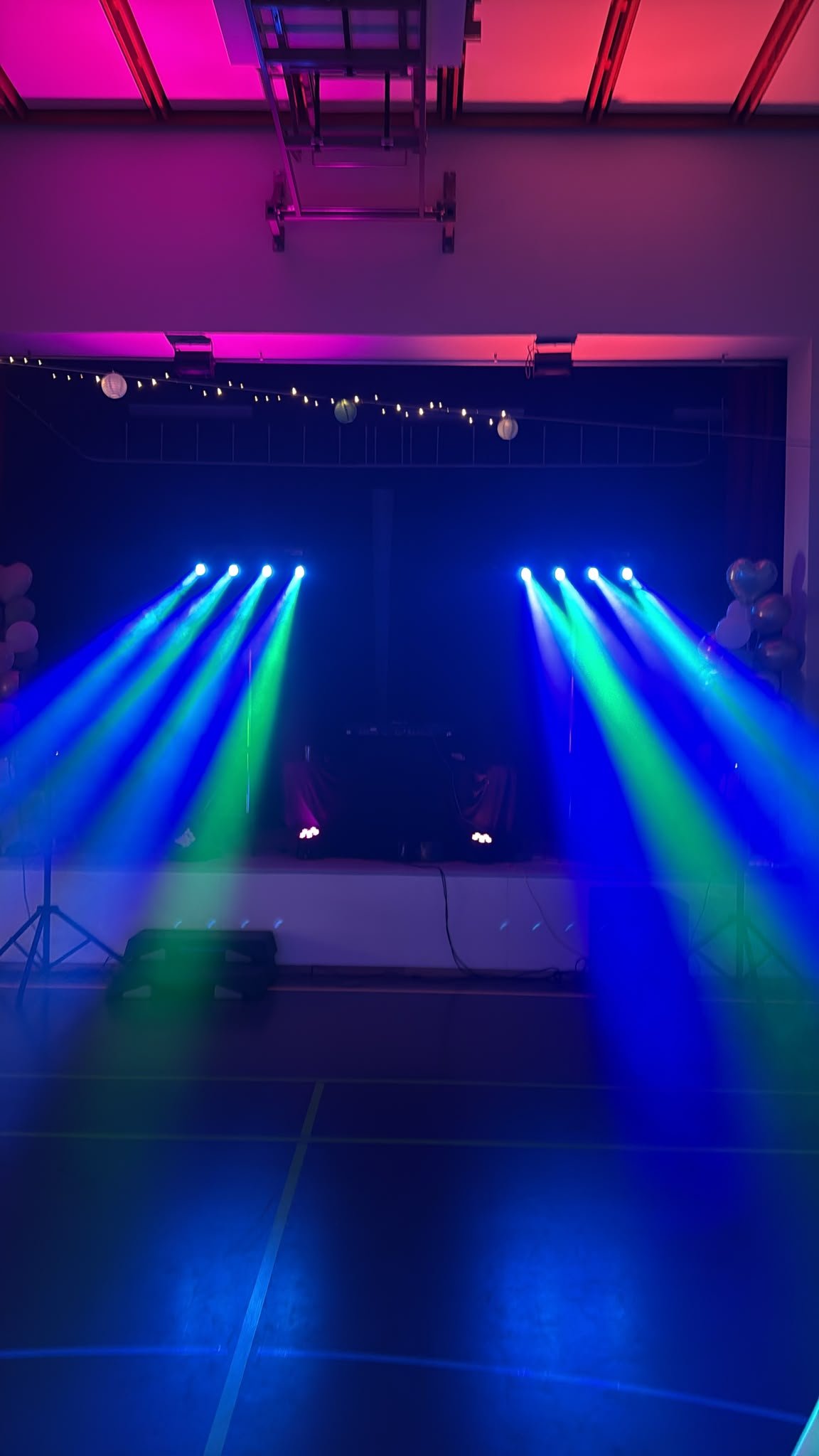 DJ-Setup mit blauen und grünen Lichtstrahlen und magentafarben beleuchteter Decke