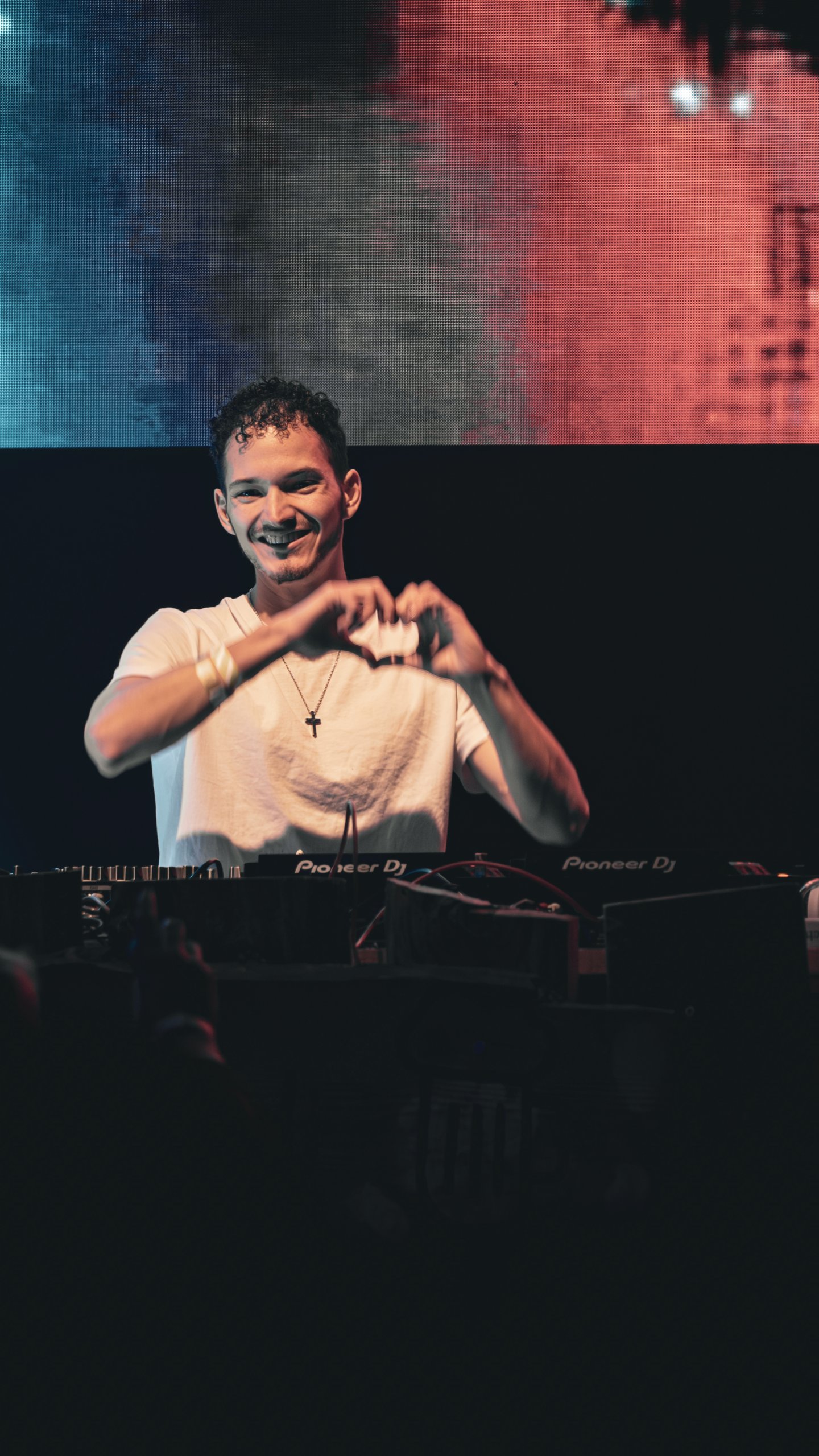 Cale lächelt am DJ-Pult und formt mit den Händen ein Herz
